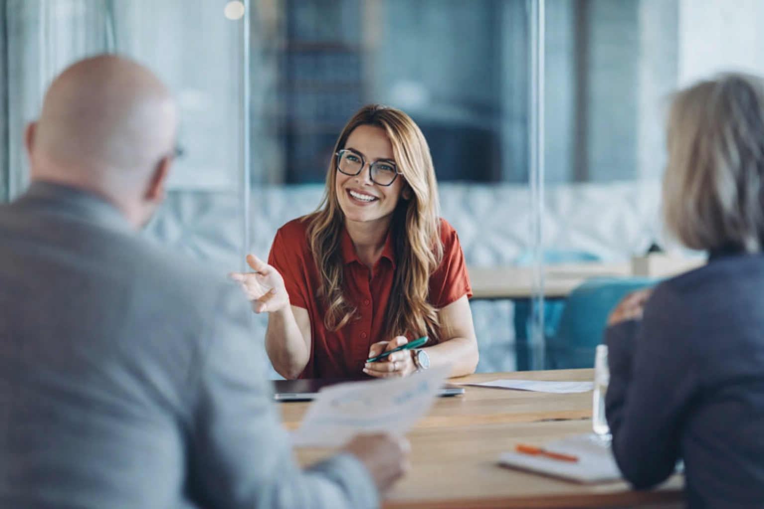 white female in glasses talking to a man and female at a conference table