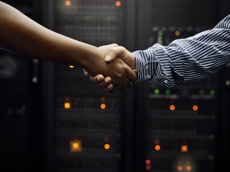 Two professionals shaking hands in front of server infrastructure to represent partnership and service.
