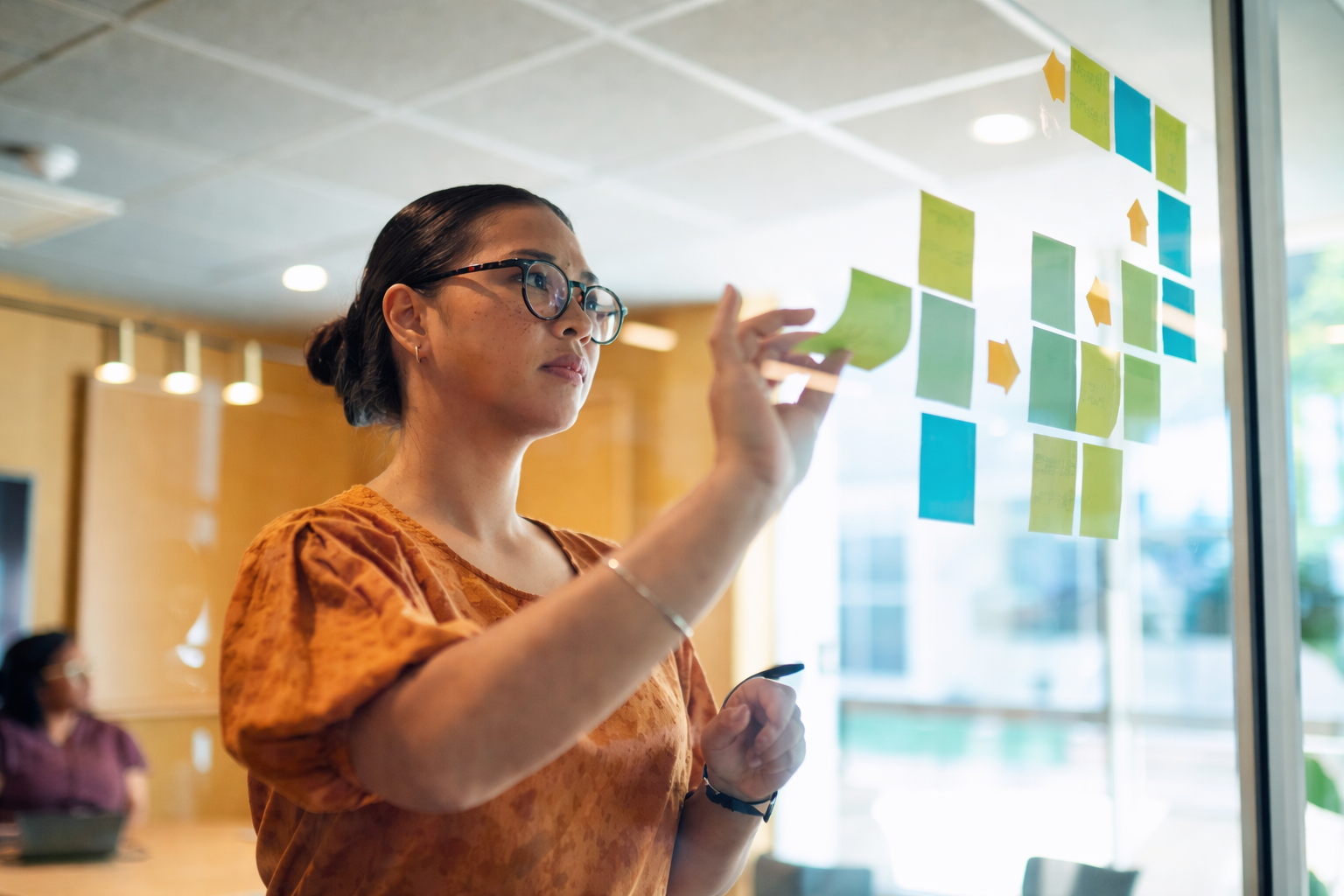 young female in glasses analyzing post-it notes on a glass window