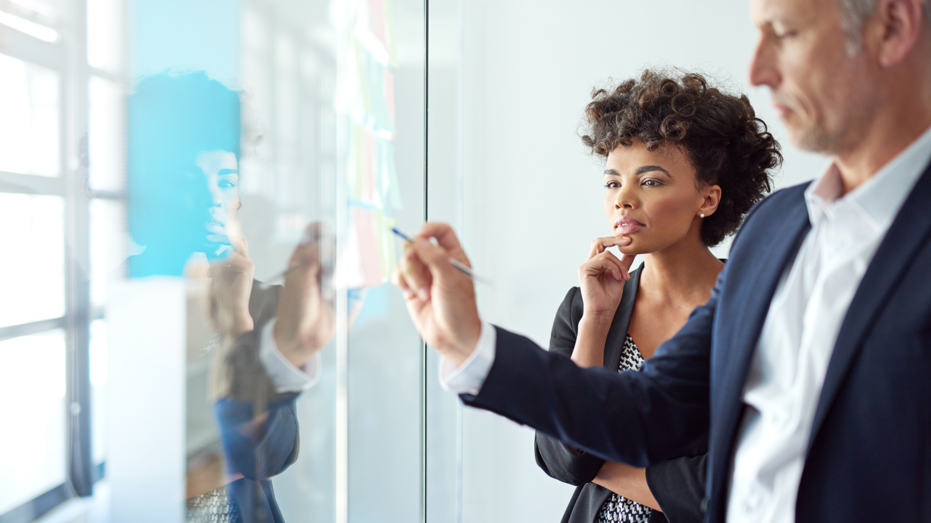 Featured image: Two professionals reviewing ideas on a glass board during a collaborative strategy session.Turning change fatigue into continuous learning and measurable adoption