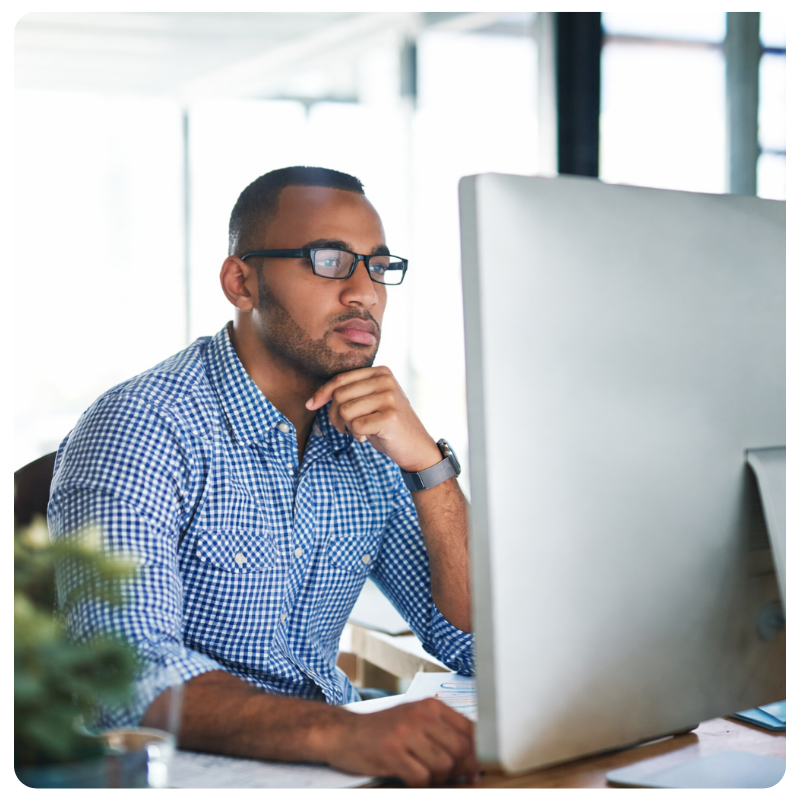 black young male in glasses looking at a computer monitor