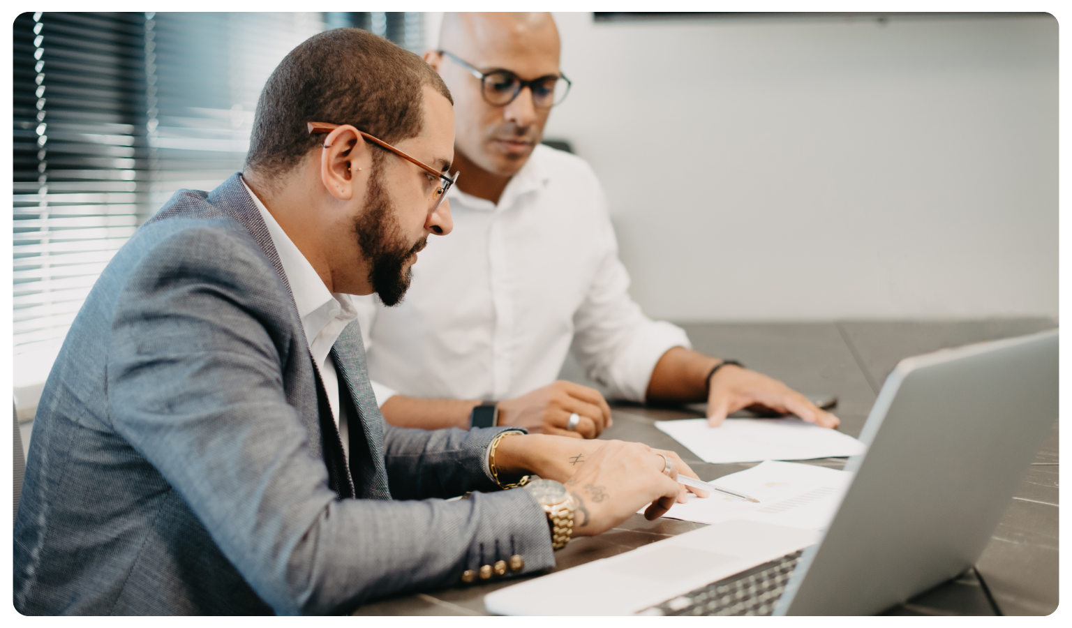 two professional men collaborating over paperwork and a laptop