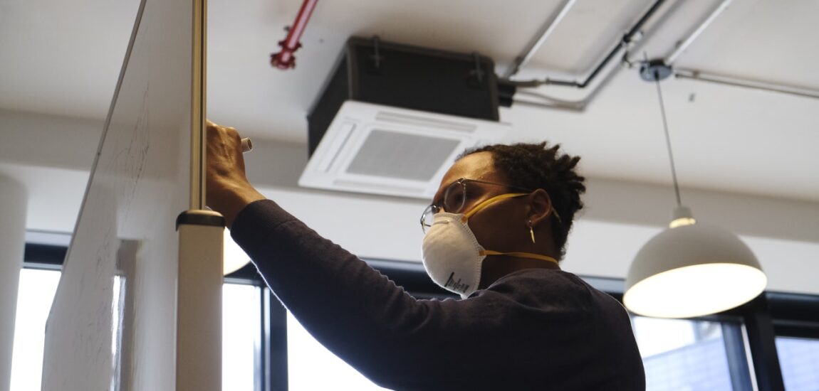 An employee wearing a mask writes on a whiteboard in an office.